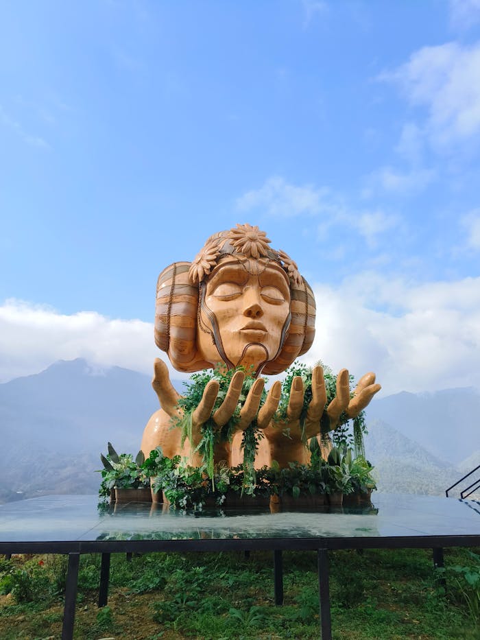 Large sculpture of serene face with mountain backdrop and clear sky.